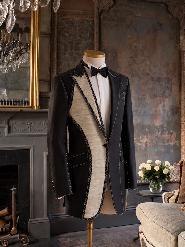 A bespoke evening jacket in progress on a dress form, one side opened to show the canvas and hand stitching, in a candlelit salon